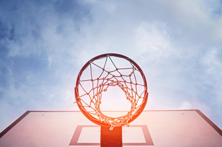 Basketball hoop on outdoor court with blue sky and clouds background