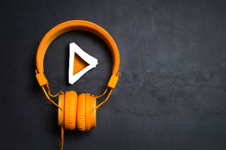 Play button and orange headphones on dark concrete backgroundの写真素材