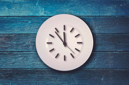 Clock on the plate on blue wooden backgroundの写真素材