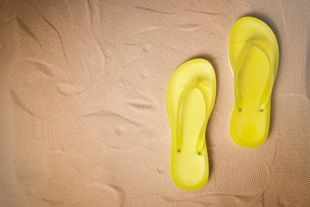 Summer holiday background with yellow flip flops on  sandy beach, top view with copy spaceの写真素材