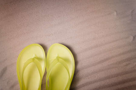 Summer holiday background with yellow flip flops on  sandy beach, top view with copy spaceの写真素材