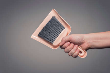 Male hand holding dustpan and brush set. Cleaning service and maintenance concept.の写真素材