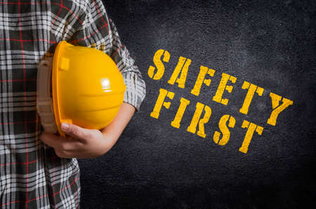 Safety first concept. Safety first stencil print on the black concrete wall. Construction worker with yellow safety helmet.の写真素材