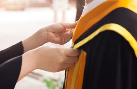 Close up of young student assisting graduation gown for other student.の写真素材