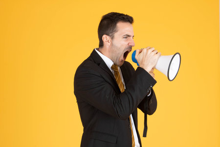 Portrait of a handsome businessman wearing white suit and tie while using megaphone, screaming with...