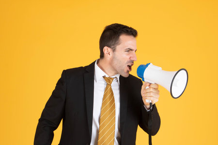 Portrait of a handsome businessman wearing white suit and tie while using megaphone, screaming with...