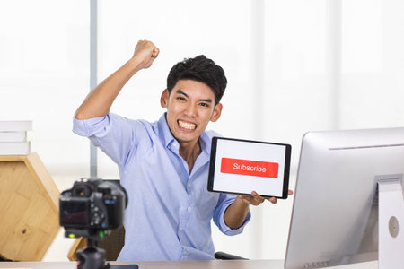 Young Asian influencer holding a table with subscribe sign while recording a video.の写真素材