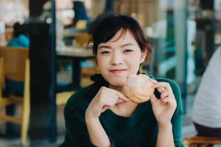Pretty Asian woman wearing green sweater and enjoyed eating Japanese Puff Cream/Shu cream.