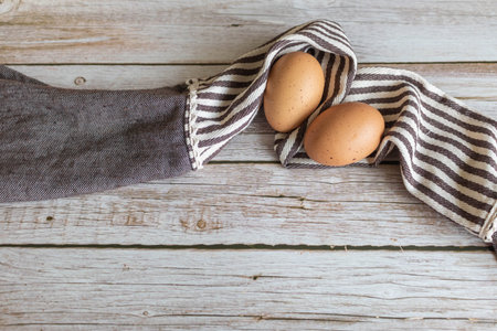 Brown chicken eggs lay on the wooden floor with brown fabric.