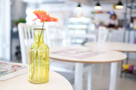 A yellow glass vase with a single orange flower in the cafe.の写真素材