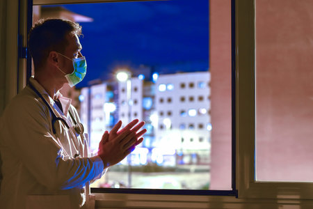 Doctor applauding people who are isolated in their homes because of the coronavirus. This is a solidarity movement started in Spain where people who are isolated go out to their windows every afternoon to thank the doctors and nurses who are fighting the disease through applause.の写真素材