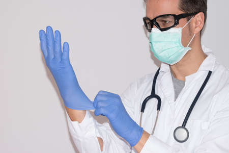 Doctor with mask and goggles wearing blue latex gloves. White background.の写真素材