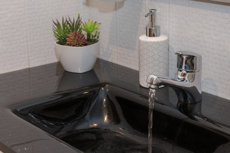Black washbasin with the water tap open for hand washing. Modern soap dish and cactus decorationの写真素材