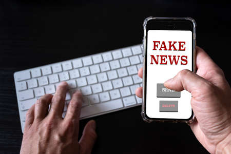 Online fake news on a mobile phone. Close up of man reading Fake news hoax or articles in a smartphone screen application. Hand holding smart device. Mockup website. Fake Newspaper portal.の写真素材