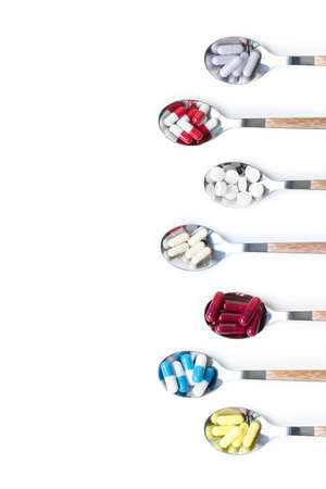 Top view variety of vitamin and mineral pills in a metal spoon with wooden handle isolated on white background, dietary supplement health product.の写真素材