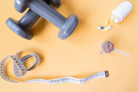 Weights and a tape measure along with pills and dietary supplements on yellow background. Sport supplements. Healthy diet concept.の写真素材