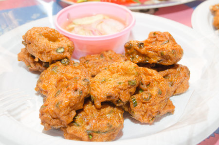 Fried fish mixed with spices, served on a plate with sauce and pickled cucumber.