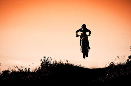 Status of silhouate motocross jumping over the amber light of sunset background.の写真素材