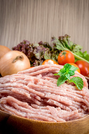 Raw ground meat in wood bowl. Minced pork on a background of fresh organic vegetables