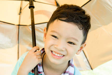 Shot of cute asian boy smiling under umbrellaの写真素材