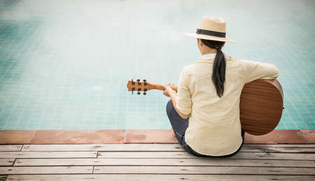 Woman playing guitar on the swimming pool.の写真素材
