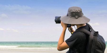 Handsome young professional photographer taking photos against blue skyの写真素材