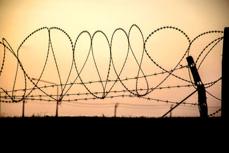 Barbed wire on dark fence. Monochrome silhouette photoの写真素材