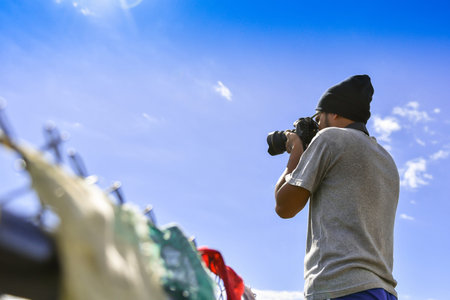 Handsome young professional photographer taking photos against blue skyの写真素材