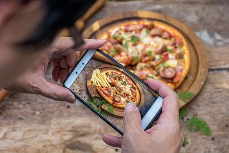 The Young man is using a smartphone to take picture of junk food on wooden.の写真素材