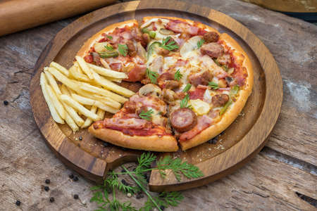 Homemade ham, salami and mushroom pizza served on a board on an old rustic wooden kitchen tableの写真素材