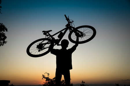 Silhouette of mountain biker holding his bike in sunsetの写真素材