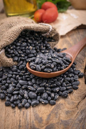 Black beans in a wooden spoon with cilantro and onions, tomato in the backgroundの写真素材