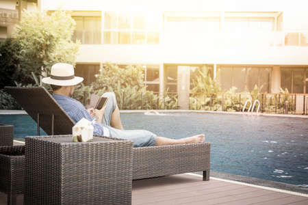 Relax in the pool. Young and successful man lying on a sun lounger at the hotel on the background of sunset.の写真素材