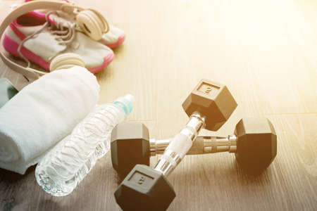 Exercise weights - iron dumbbell with extra plates on a wooden deck, Sport equipment. Sneakers, water, towel, earphones and phone on wooden backgroundの写真素材