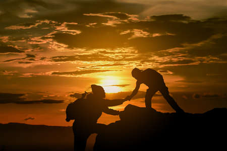 Two friends helping each other and with teamwork trying to reach the top of the mountains during wonderful summer sunset.の写真素材