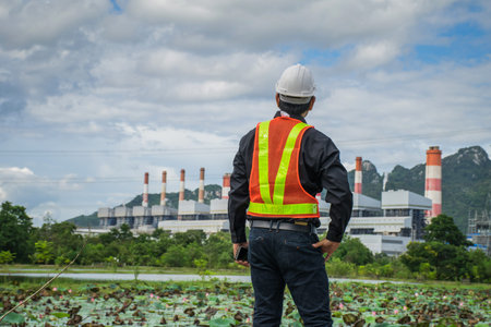 Engineer with a coal power plant in the background, Thailand.