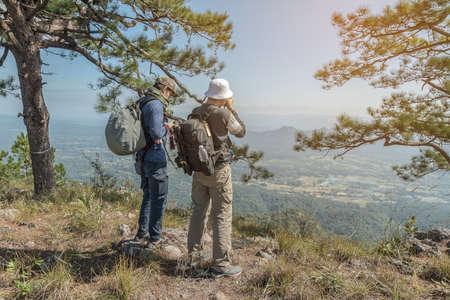 Photographer with camera in hand on top of mountain. Hiker climbed on peak of rock above foggy valley.の写真素材