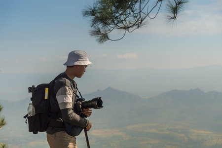 Photographer with camera in hand on top of mountain. Hiker climbed on peak of rock above foggy valley.の写真素材