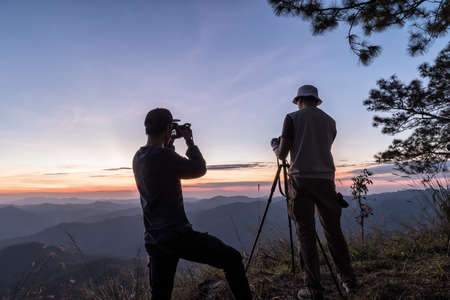 Hiker with camera on tripod takes picture from rocky summit. Thailand.の写真素材