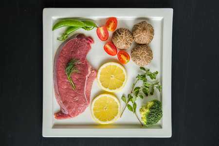 Raw steaks of veal,prepared for roasting, steak meat with salad on a black wooden backgroundの写真素材