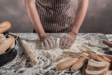 Man preparing buns at table in bakery, Man sprinkling flour over fresh dough on kitchen tableの写真素材