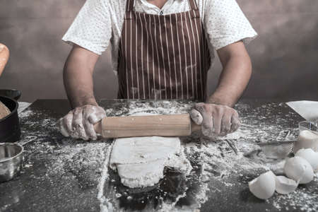Man preparing buns at table in bakery, Man sprinkling flour over fresh dough on kitchen tableの写真素材