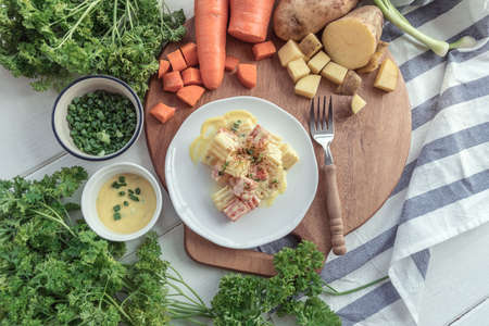 Traditional German potato salad with carrot, onion and mayonnaise, Hand of chef adds salad to potato wedges on plateの写真素材