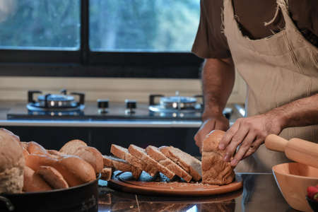 Man preparing buns at table in bakery, Man sprinkling flour over fresh dough on kitchen tableの写真素材