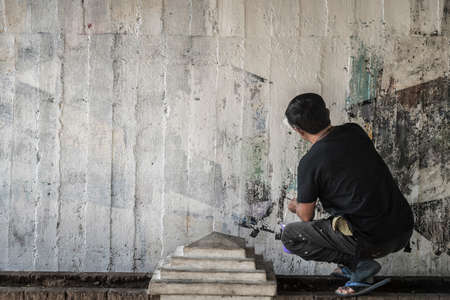 Young man clean the walls by painting white over the old cement wall, Thailand.の写真素材