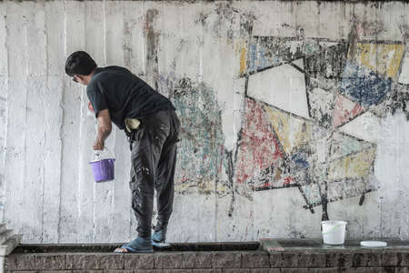 Young man clean the walls by painting white over the old cement wall, Thailand.の写真素材