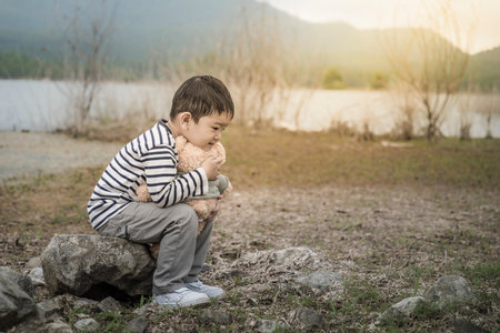 child asian with teddy bear sitting site the reservoir is the background.Thailand.の写真素材