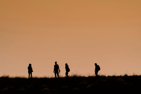 Silhouettes of hikers with backpacks enjoying sunset view from top of a mountain, Silhouette...