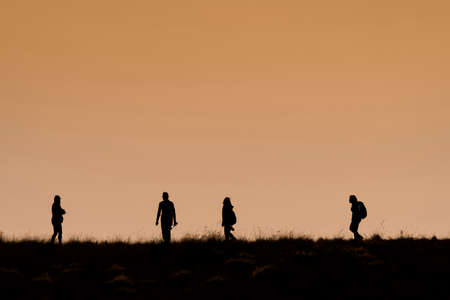 Silhouettes of hikers with backpacks enjoying sunset view from top of a mountain, Silhouette tourists and photographers with beautiful sunriseの写真素材