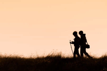 Silhouettes of hikers with backpacks enjoying sunset view from top of a mountain, Silhouette tourists and photographers with beautiful sunriseの写真素材